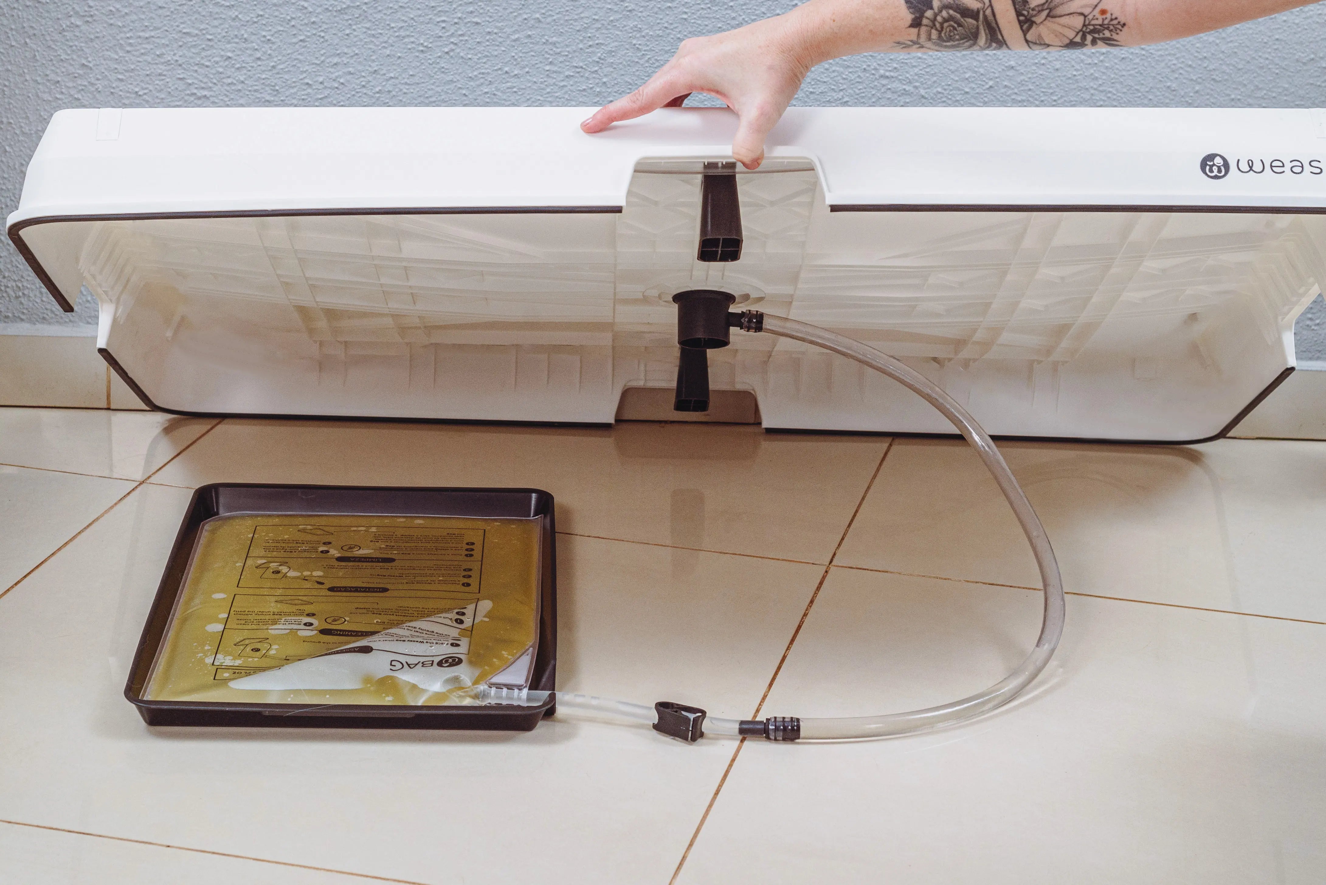 Image showing the Weasy Bag positioned underneath the tray. The bag rests on the bag tray and connects to a hose that leads to the drain.