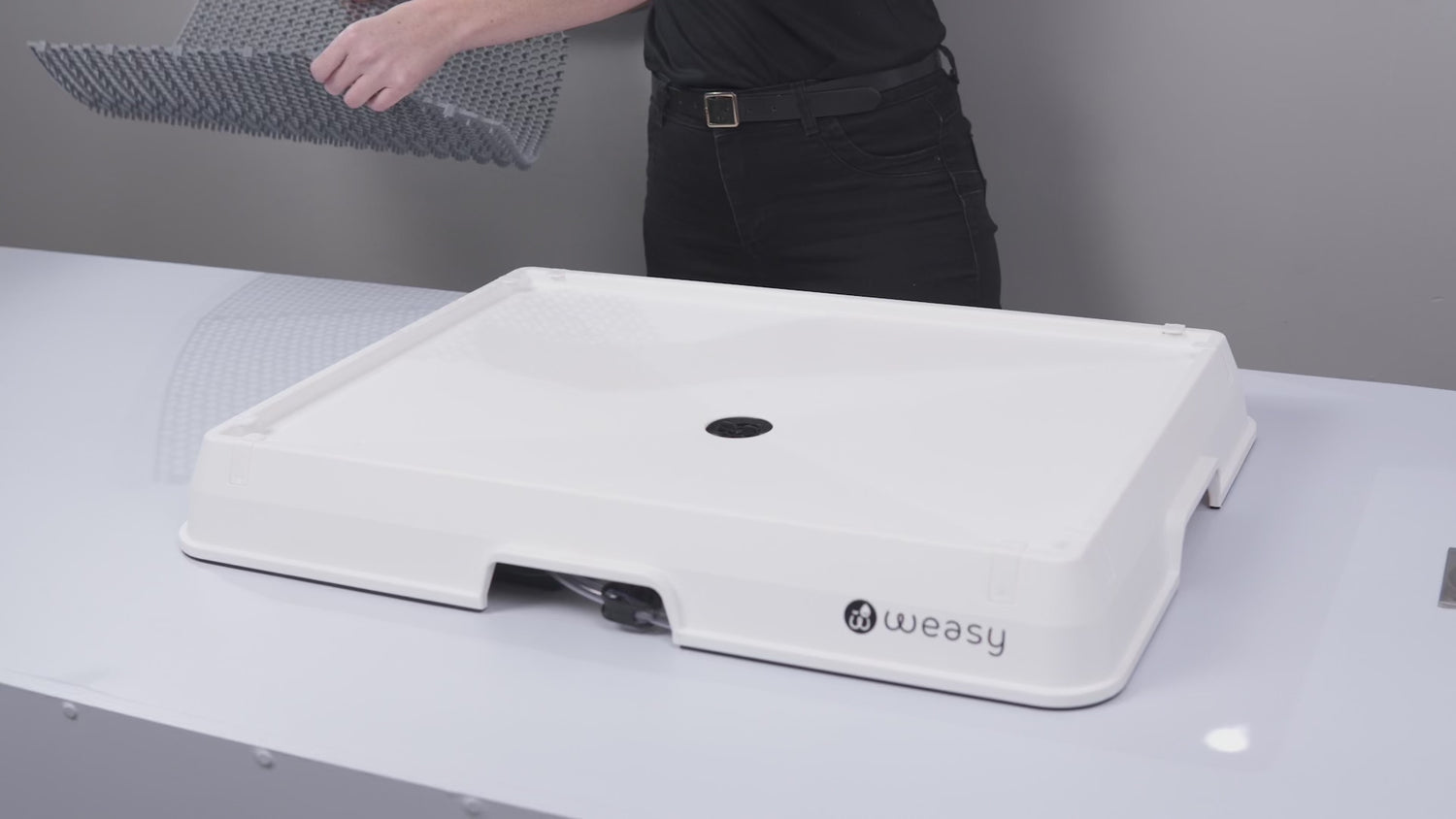 Video showing the elevated mat being placed on top of the Weasy Smart Potty platform. Next, a liquid simulating urine, followed by water, is poured down the drain. The fluids flow through the system and collect in the Weasy Bag located beneath the tray.